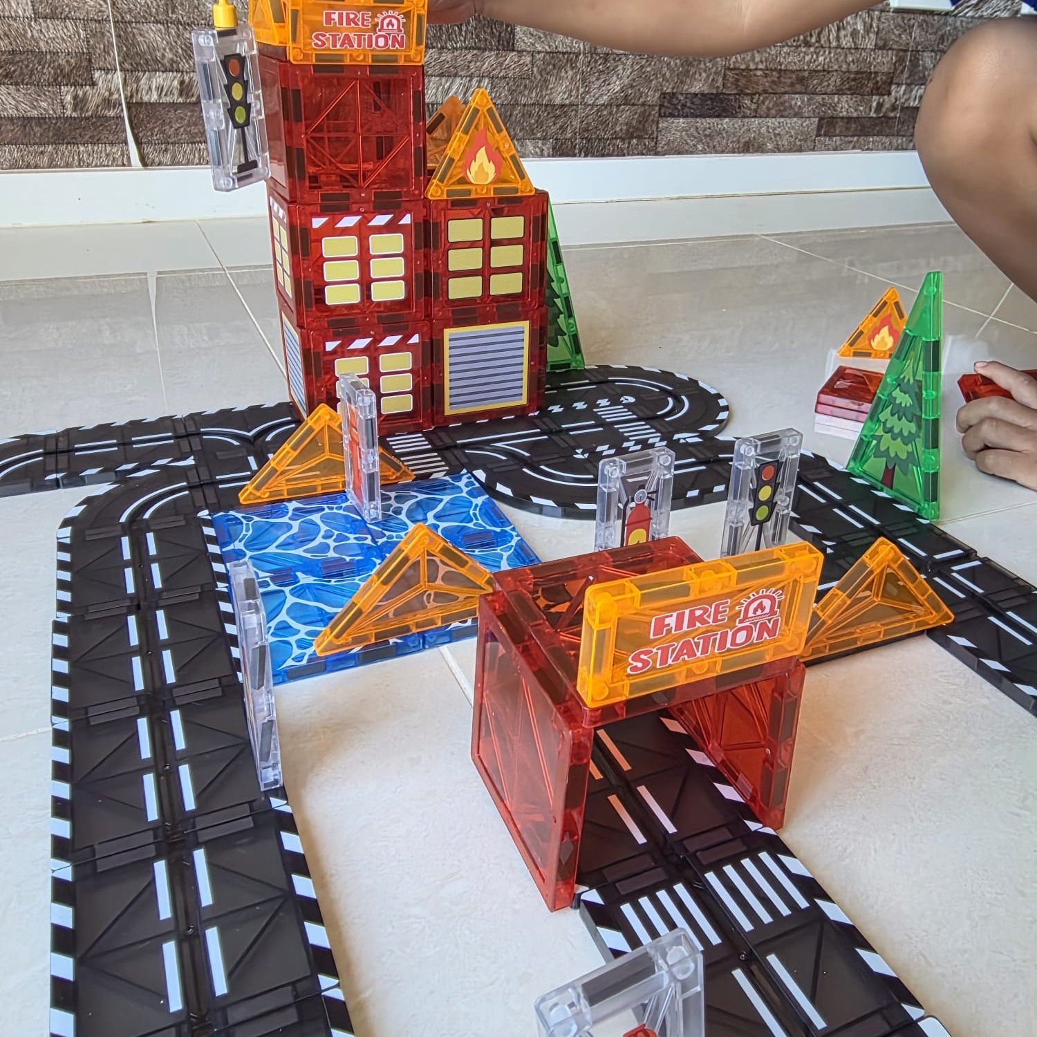 Toy fire station set with a child's hand interacting with it on a track layout.